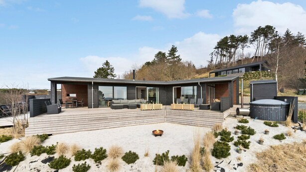 Une maison moderne dotée d’une grande terrasse, d’un espace salon extérieur et d’un foyer.