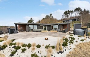 Een modern huis met een ruim terras, buitenmeubels en een vuurkorf.