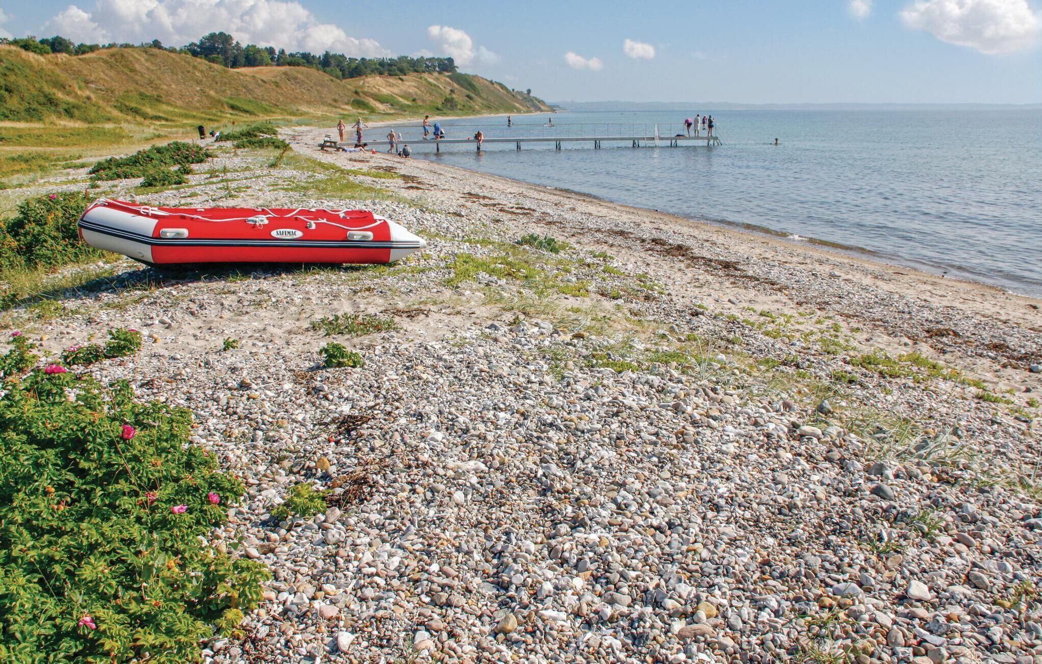 Een rotsachtig strand met een rode boot waarop 'SAFEMAC' staat en een pier die het water in reikt.
