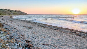 Une plage avec une jetée qui s’avance dans la mer, un rivage rocheux et un coucher de soleil en arrière-plan.
