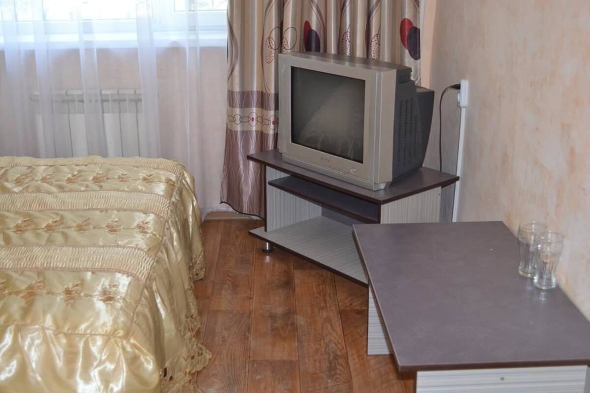 A bedroom with a bed, a television on a stand, and a small table with glasses.