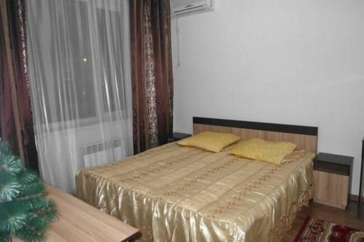 A bedroom with a bed, curtains, an air conditioning unit, a nightstand, and a small table.