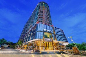 A modern hotel with a curved facade, large glass windows, and a prominent signage. - Ding Shang Service Apartment Hotel (Shenzhen)