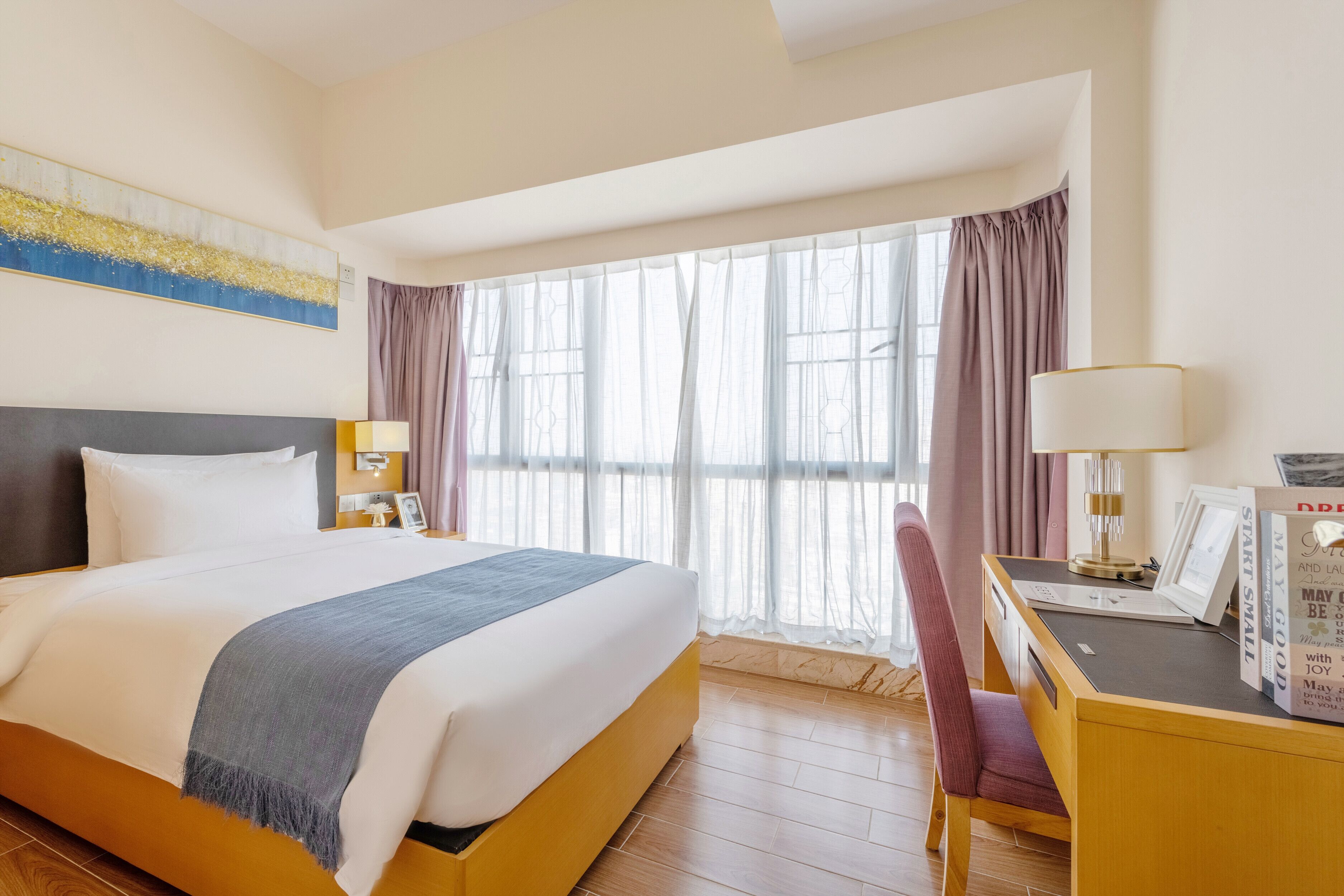 Habitación de hotel con una cama grande, un escritorio con lámpara, una silla y una ventana con cortinas.