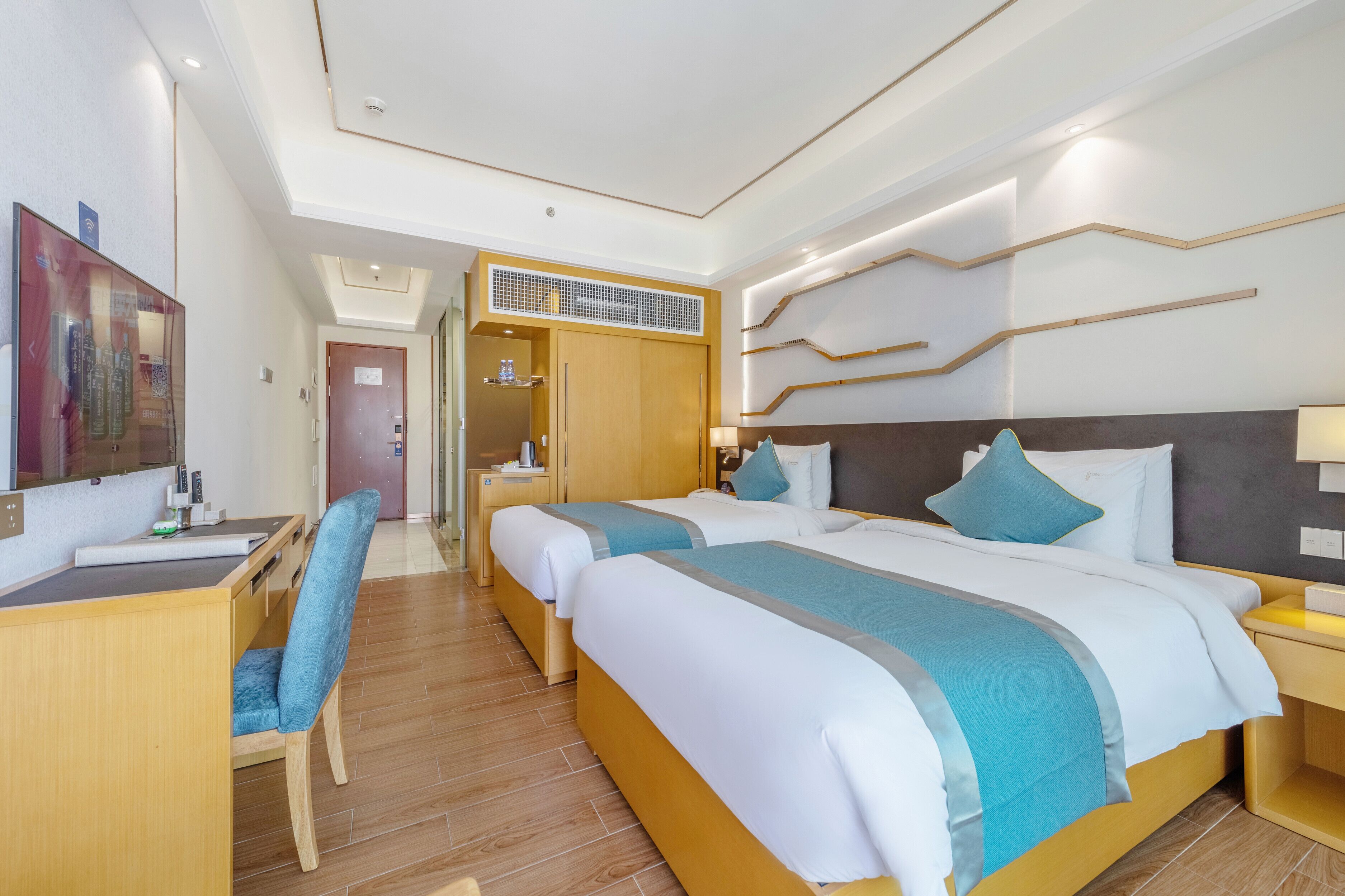 A hotel room with two beds, a desk, and a chair. There is a wardrobe and a door leading to another room.
