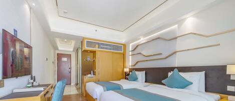 A hotel room with two beds, a desk, and a chair. There is a wardrobe and a door leading to another room.