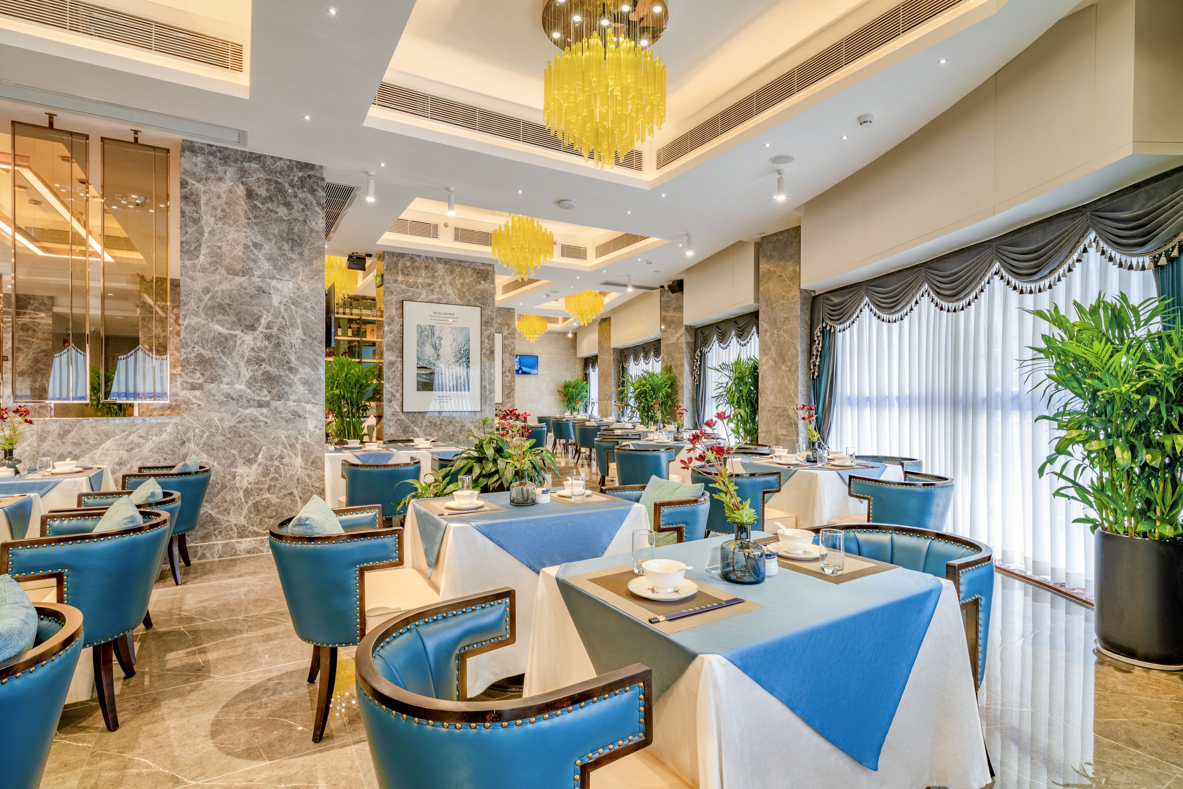 A restaurant with blue upholstered chairs, marble walls, and yellow chandeliers.