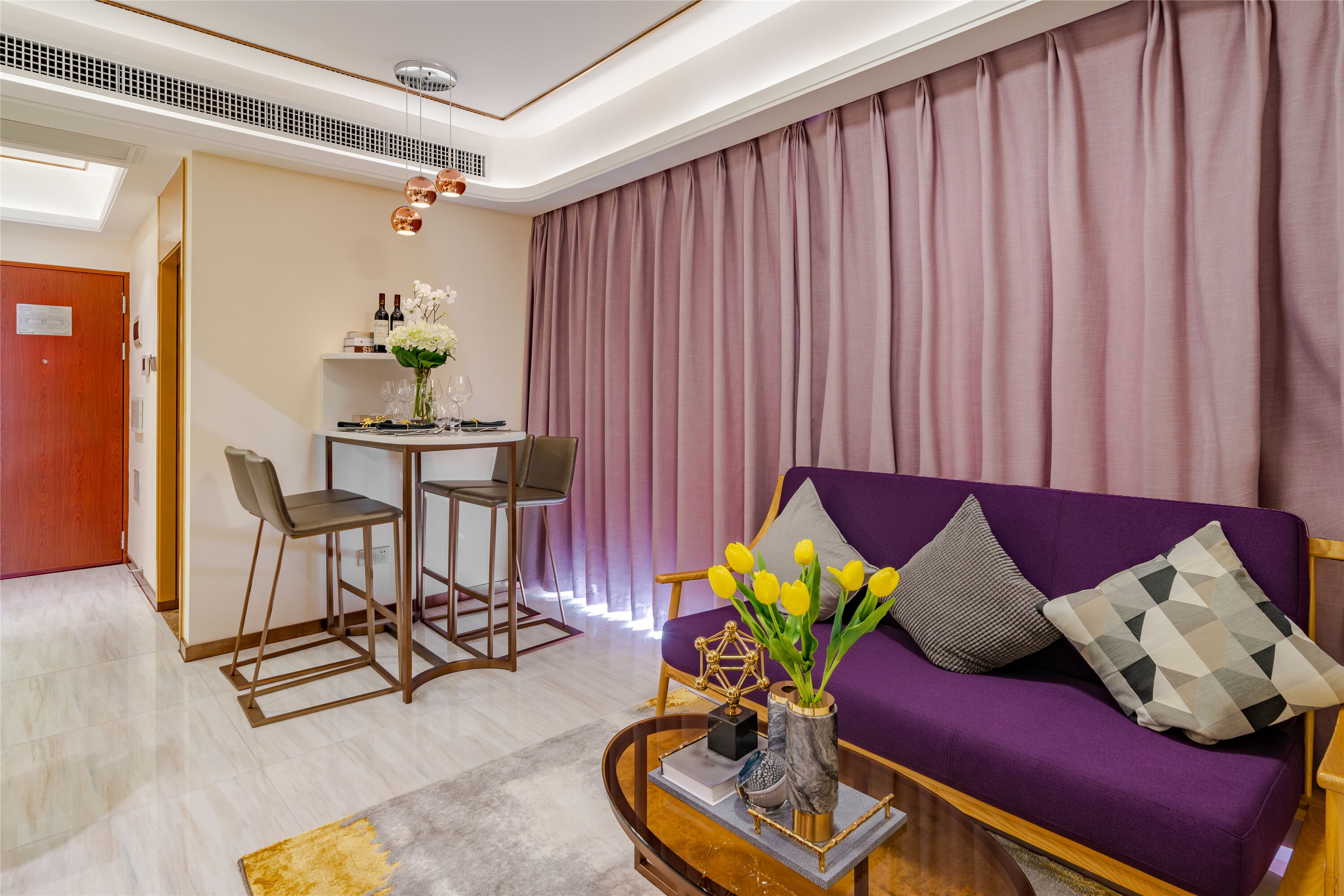 A modern living room with a purple sofa, a coffee table with a vase of flowers, and a dining area with chairs and a small table.