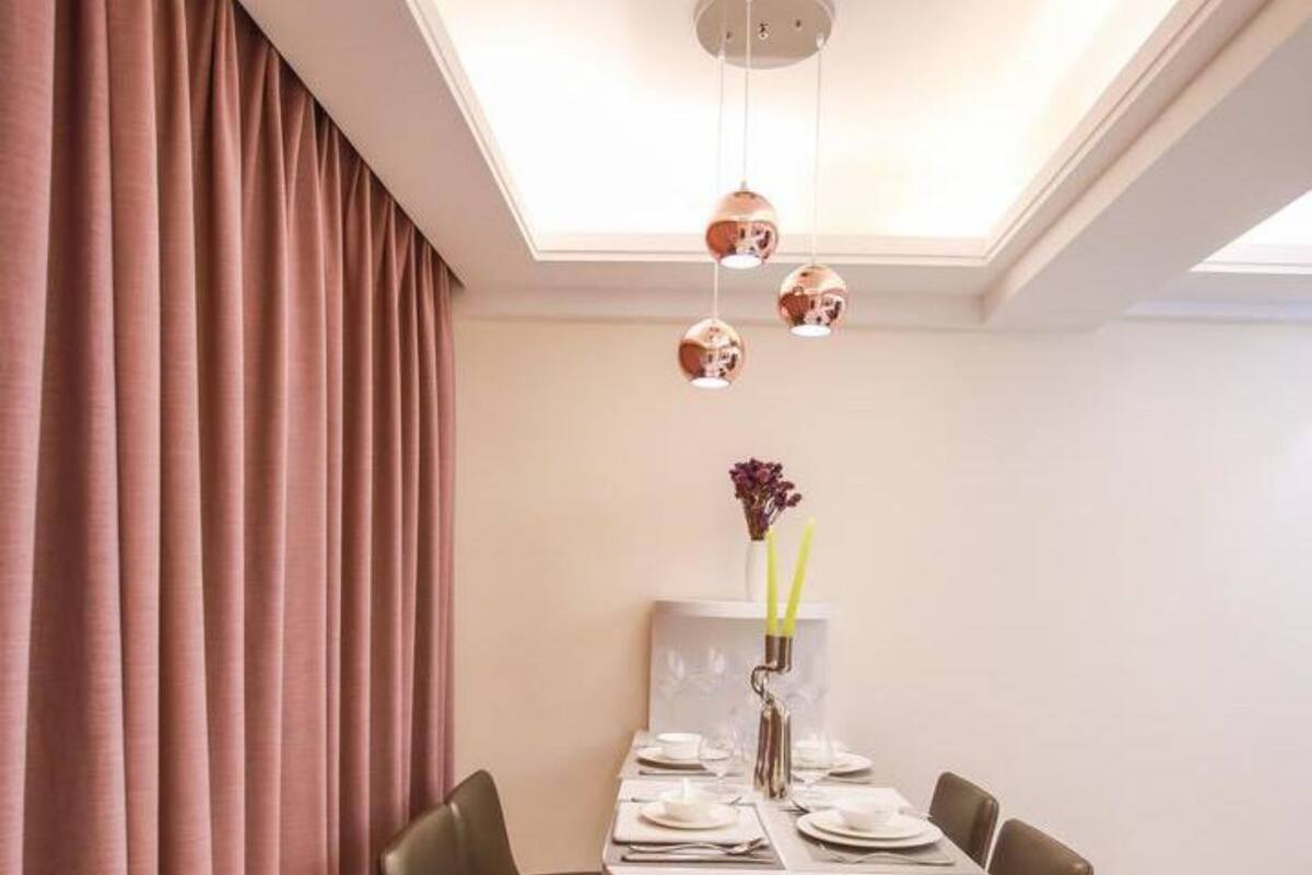 Uma sala de jantar com uma mesa redonda, duas cadeiras, um vaso com flores e luminárias pendentes.