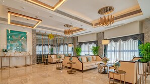 Eine großzügige Lobby mit modernem Design, ausgestattet mit einer geräumigen Sitzecke, einem Empfangstresen und einem großen Fenster mit Vorhängen.