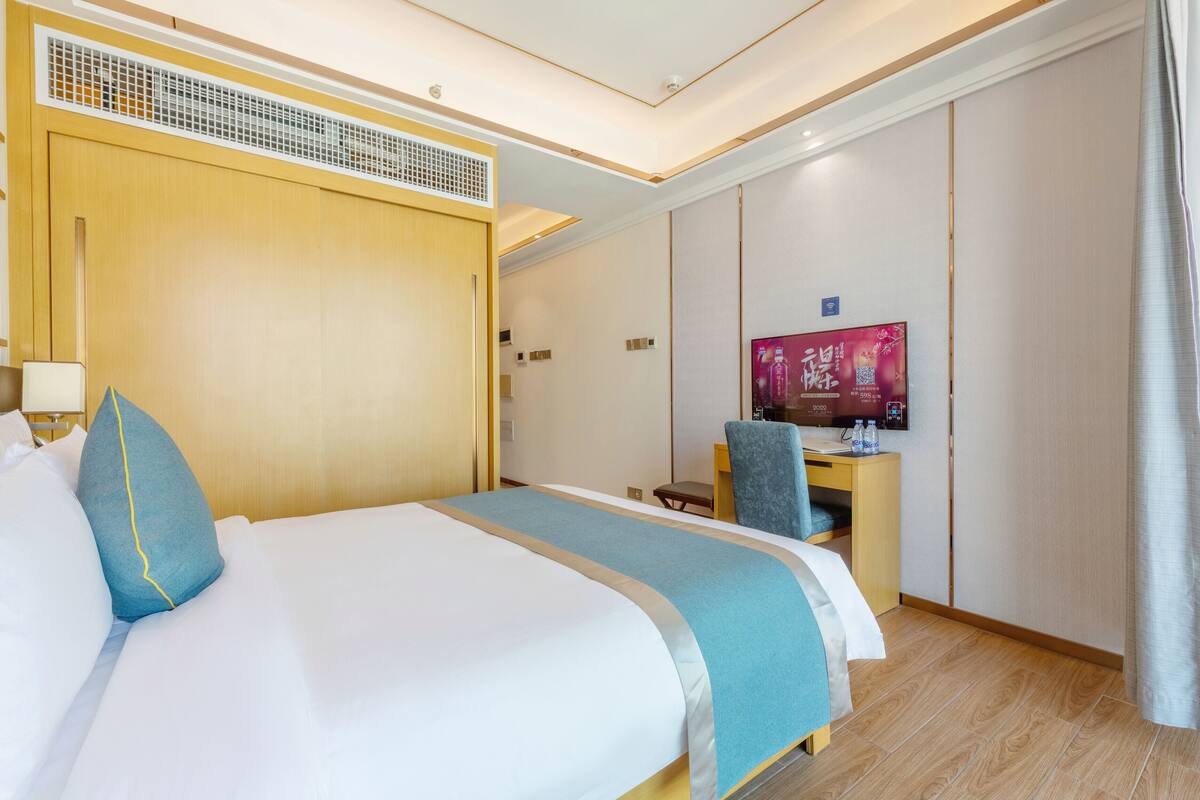 Quarto de hotel com uma cama grande, uma escrivaninha, uma televisão e um guarda-roupa.