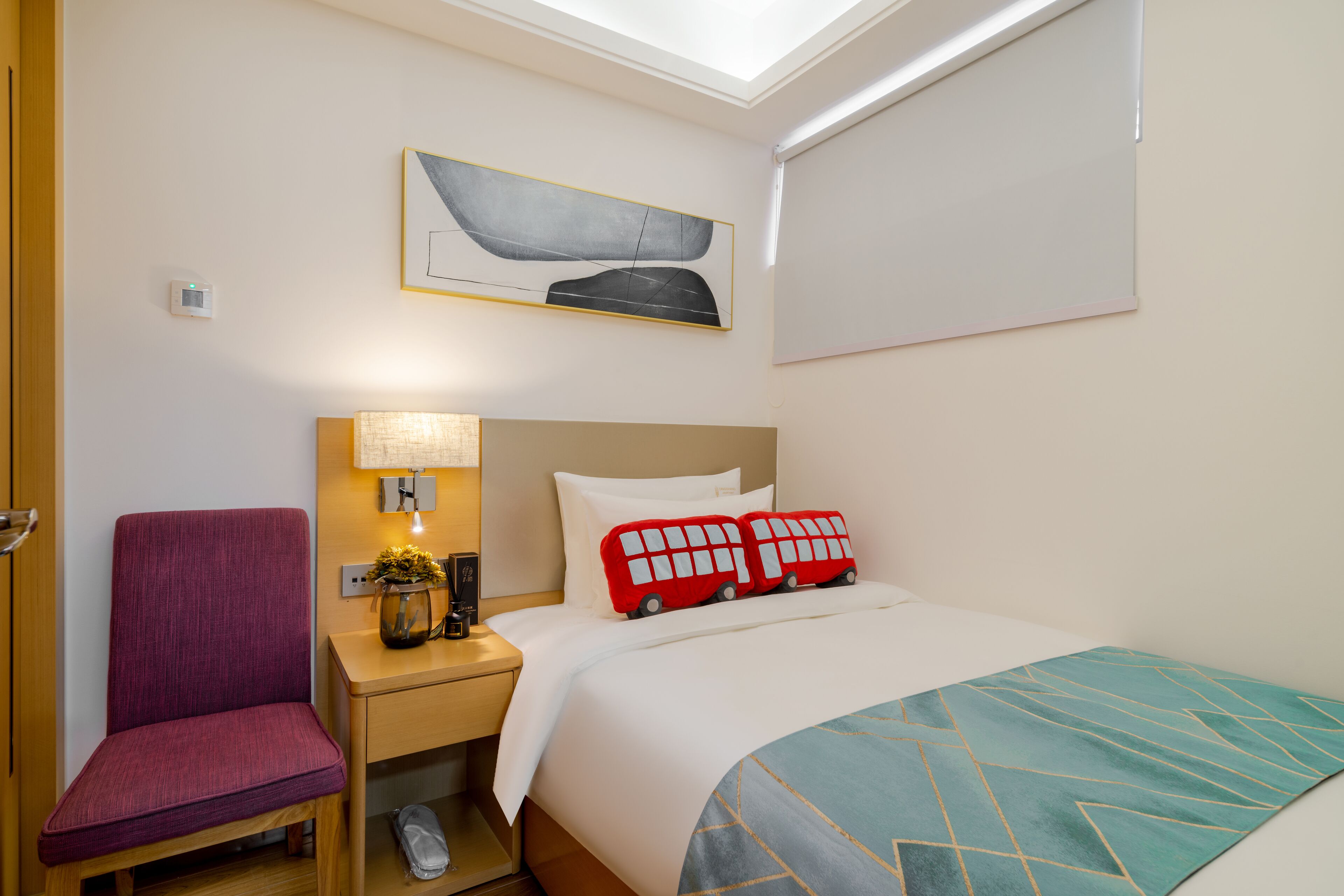 Habitación de hotel con cama, una silla, una mesita de noche con lámpara, un cuadro en la pared y ventana.