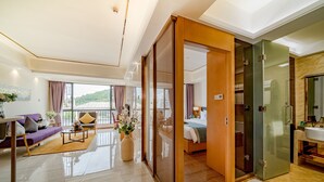 Ein modernes Hotelzimmer mit Balkon, einer Couch, einem Esstisch und einem großen Fenster.