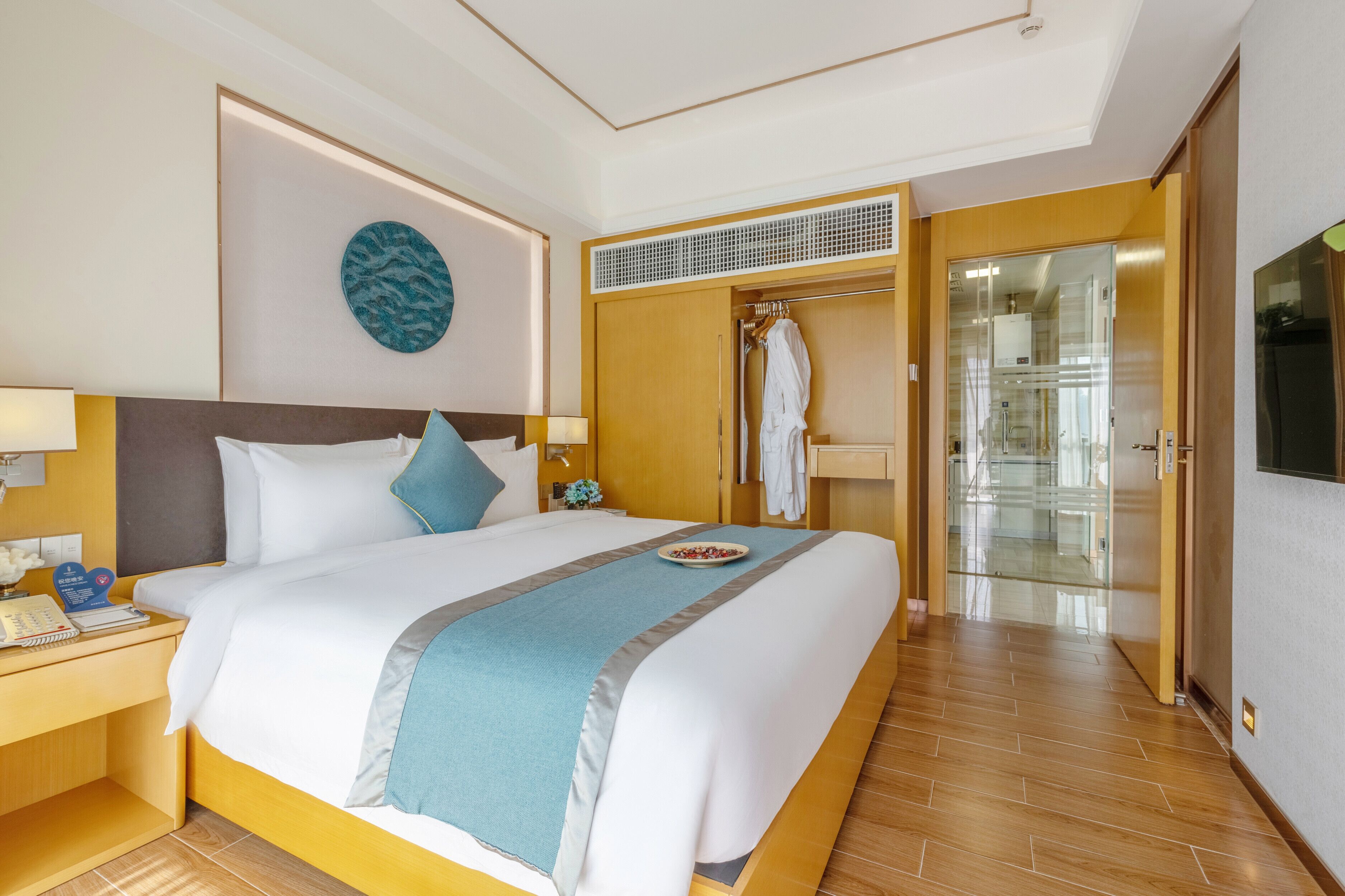 A hotel room with a large bed, a bedside table with a lamp, a wardrobe, and a bathroom visible through an open door.