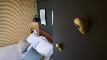 A hotel room with a bed, pillows, a headboard, a wall-mounted light, and a decorative golden heart on the wall.