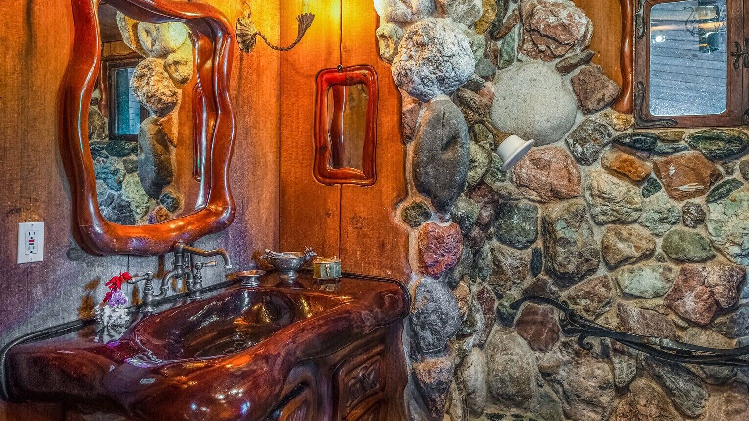Een badkamer met een houten wastafelmeubel, een grote spiegel en een stenen muur.