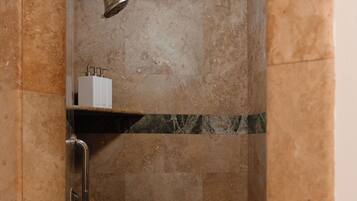 A shower with a handheld showerhead, a shelf with toiletries, and a marble-tiled wall.