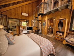 Un dormitorio de cabaña de madera con cama, televisión, escalera y zona de comedor.