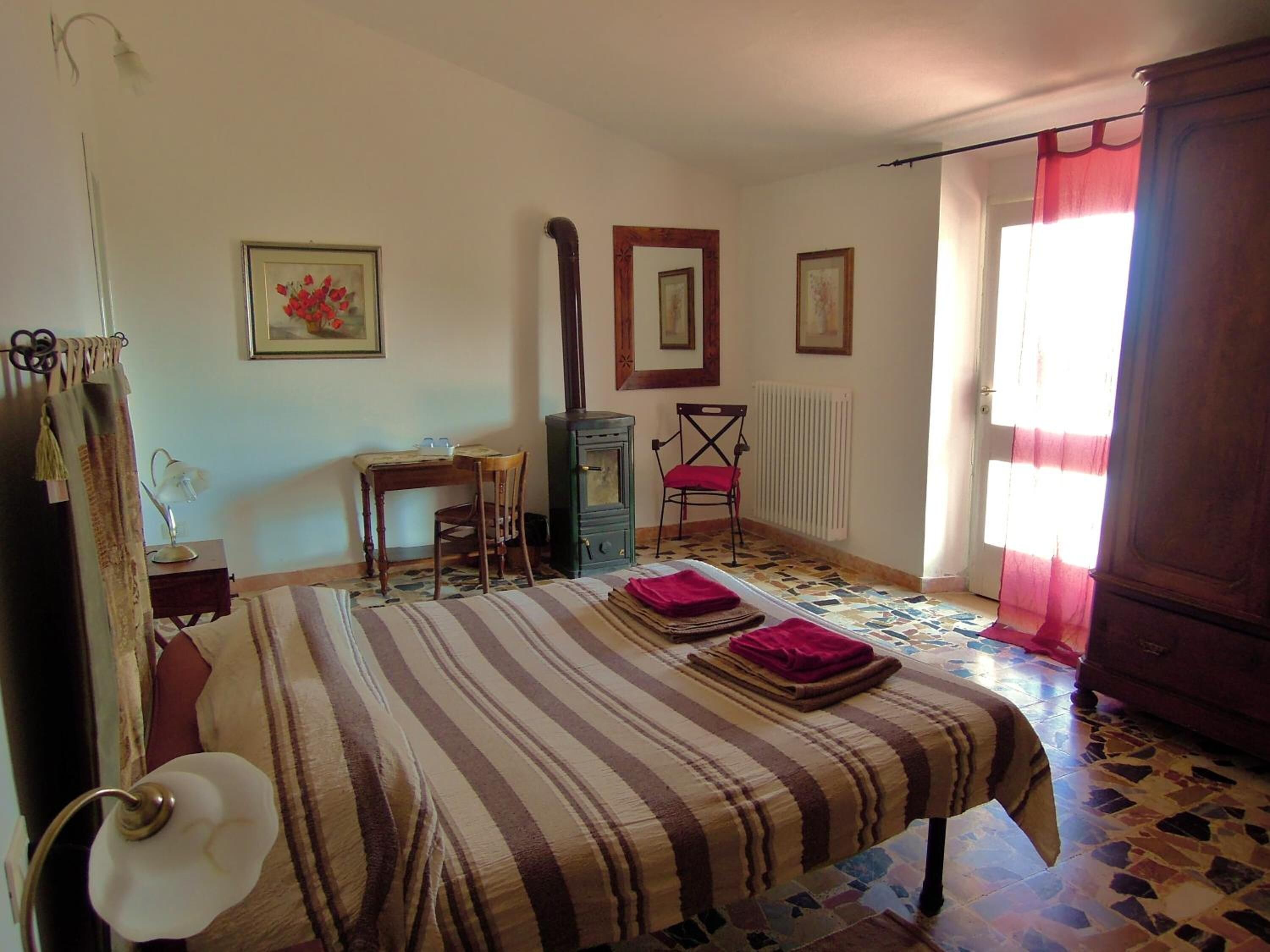 Quarto com cama, escrivaninha, cadeira, radiador e janela com cortinas.