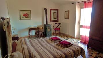 Quarto com cama, escrivaninha, cadeira, radiador e janela com cortinas.
