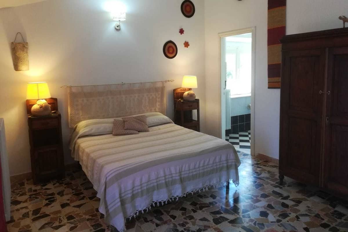 Une chambre à coucher avec un lit, deux tables de chevet avec des lampes, une armoire en bois et un plancher carrelé.