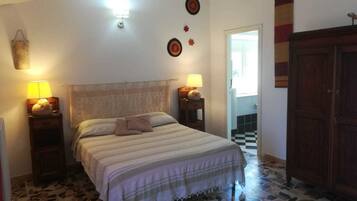 Un dormitorio con cama, dos mesitas de noche con lámparas, un armario de madera y suelo de baldosas.