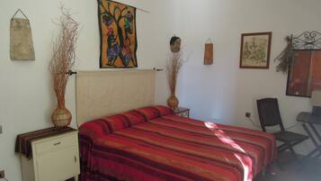 A bedroom with a bed, a nightstand, a chair, and wall decorations including a painting and two vases.