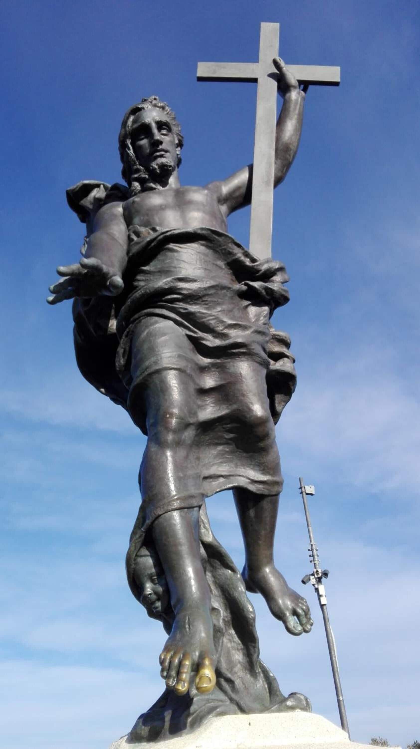 A statue of a figure holding a cross, with a clear sky in the background.