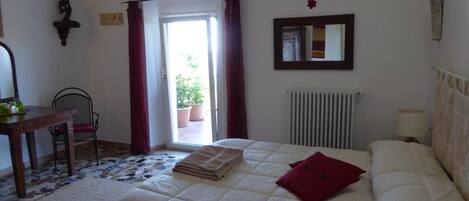 A bedroom with a bed, a desk, a chair, a radiator, and a window with curtains.