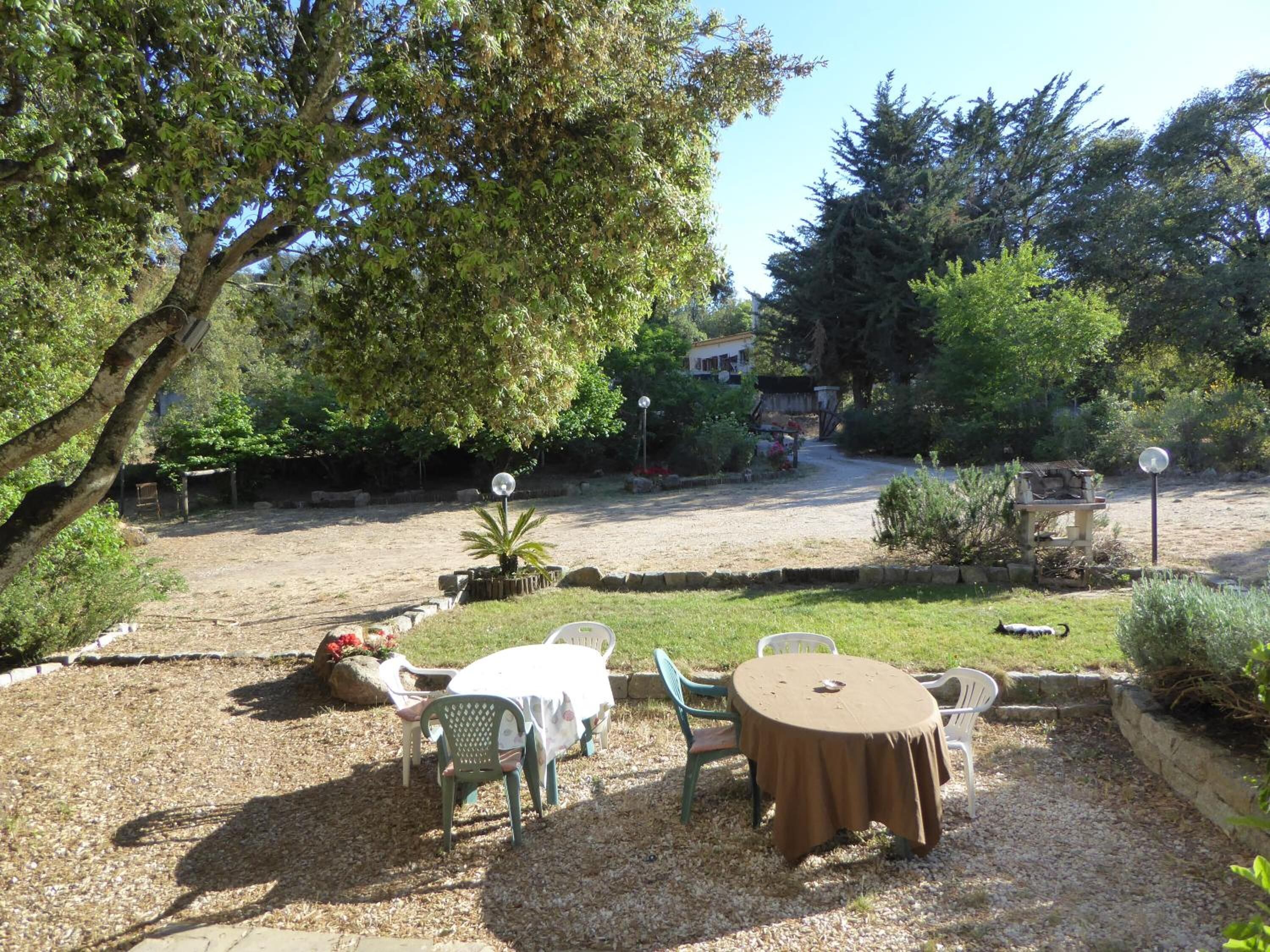 An outdoor patio area with a round table and chairs, surrounded by gravel and greenery.