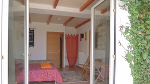 Un dormitorio con cama, puerta de madera, cortina roja y una silla.