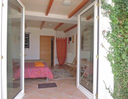 Un dormitorio con cama, puerta de madera, cortina roja y una silla.