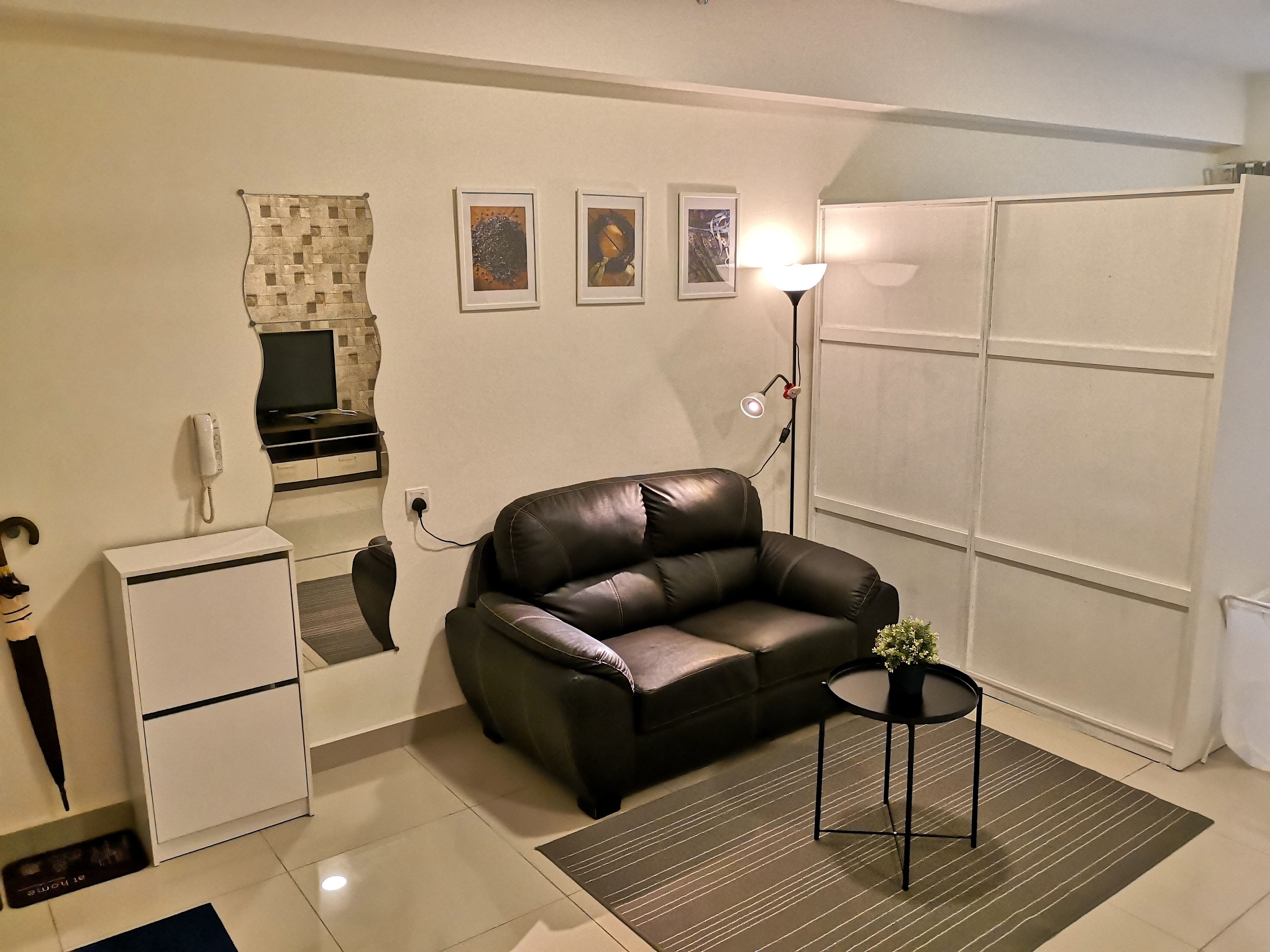 Un espacio habitable compacto con sofá, una mesita con una planta, refrigerador, televisor y teléfono en la pared.