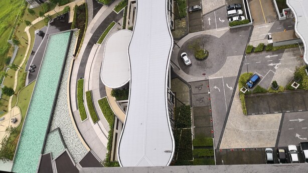 Vista aérea de un edificio moderno con un techo curvo distintivo, rodeado de una zona de estacionamiento y zonas verdes.