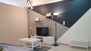 Una sala de estar moderna con una cama, un televisor, una mesita de centro y una lámpara de pie.