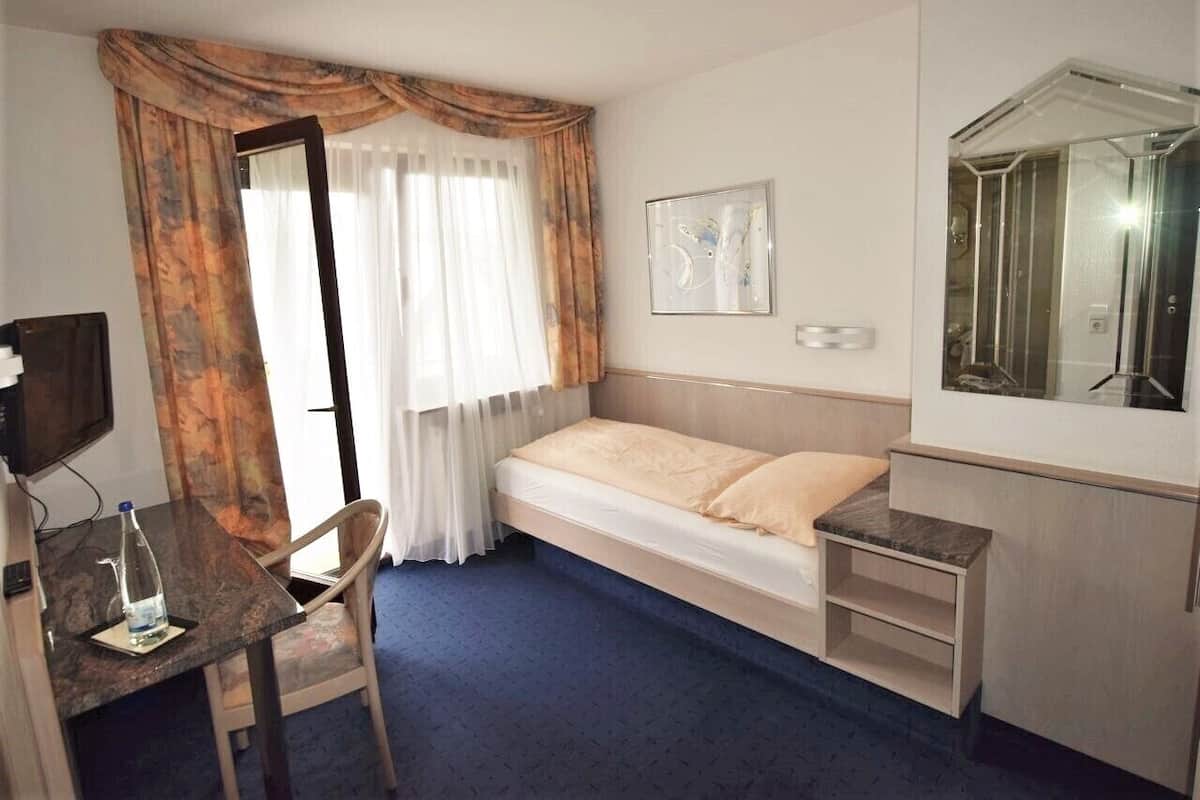 Ett hotellrum med en säng, ett skrivbord med en stol, en spegel och ett fönster med gardiner.