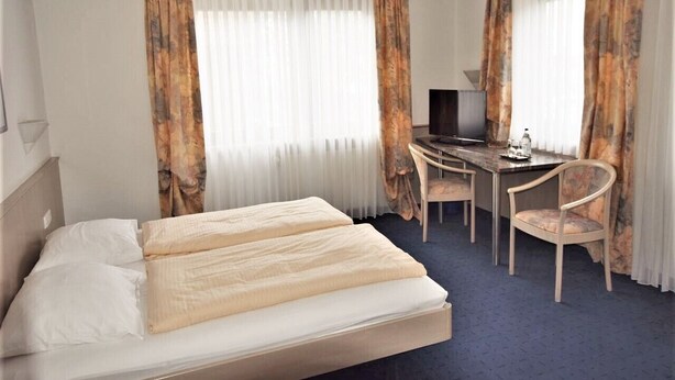 A hotel room with a bed, a desk, and a chair. - Hotel Alena (Filderstadt)