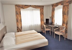 Et hotelværelse med en seng, et skrivebord og en stol.
