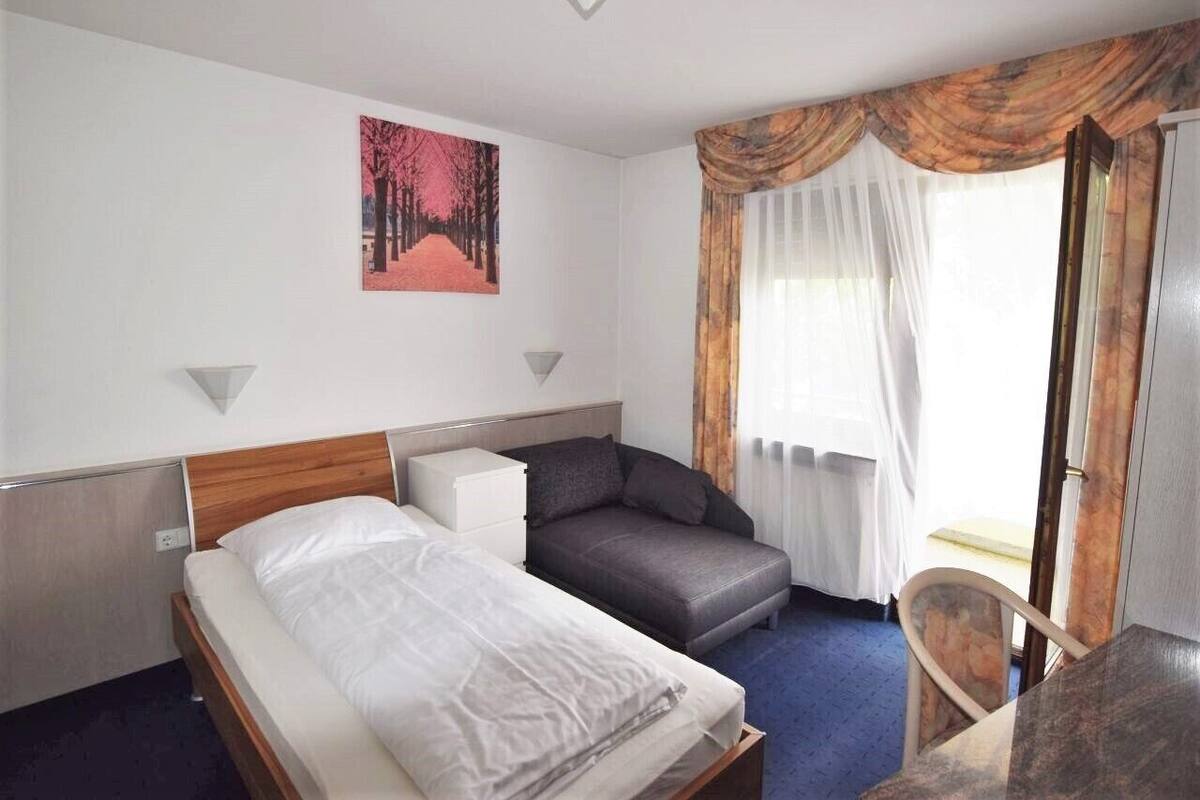 Ett hotellrum med en säng, en soffa, ett litet bord och ett fönster med gardiner.