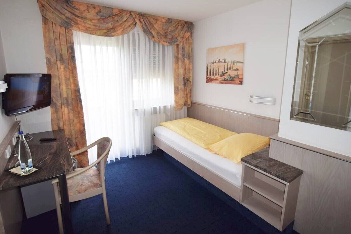 Ett hotellrum med en säng, ett skrivbord, en stol, en tv och en tavla på väggen.