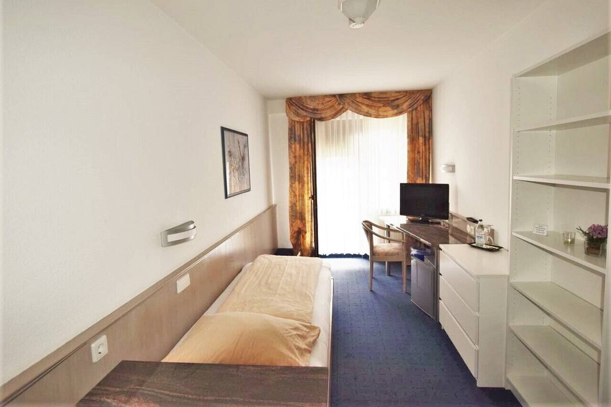 Ett hotellrum med en säng, ett skrivbord med en dator, en tv och en garderob.