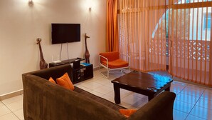 A living room with a sofa, a coffee table, a TV, and a giraffe statue. - Barizi Holiday Apartments (Mtwapa)