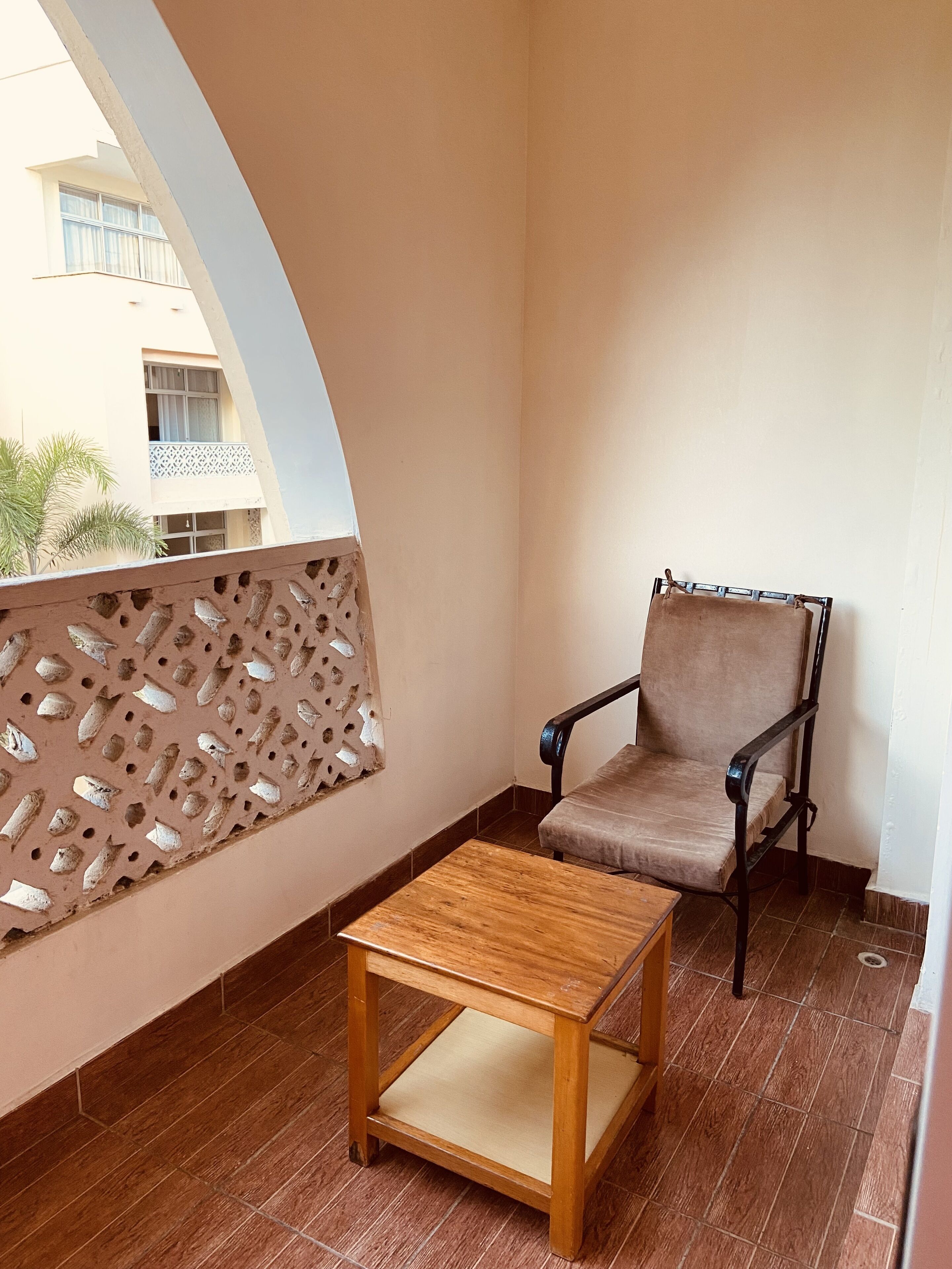 A balcony with a chair and a small table, a perforated wall, and a view of buildings.