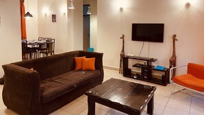 A living room with a brown sofa, a coffee table, a TV, and two giraffe statues. - Barizi Holiday Apartments (Mtwapa)