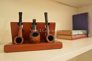 A wooden pipe rack with three pipes and a stack of books on a shelf.
