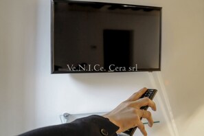 Une main tenant une télécommande devant un téléviseur fixé au mur.
