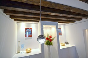 A modern interior with exposed wooden beams, a hanging mirror, and a display of decorative items including a vase with red flowers.
