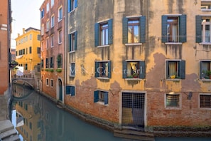 A canal-side building with multiple windows and balconies, reflecting in the water.