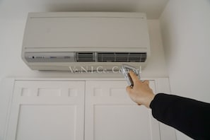 A hand holding a remote control near a white air conditioning unit mounted on a wall above a white door.
