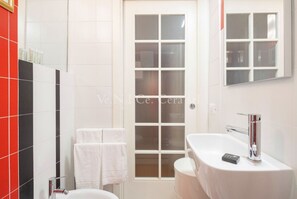 Une salle de bain avec un lavabo blanc, un miroir et une porte dotée d’un panneau en verre dépoli.